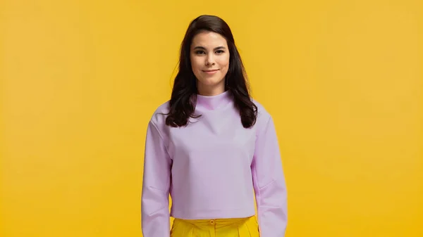 Alegre joven mujer en sudadera púrpura de pie y mirando a la cámara aislada en amarillo - foto de stock