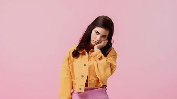 Незадоволена молода жінка в помаранчевій джинсовій куртці дивиться на камеру ізольовано на рожевому — стокове фото