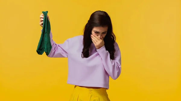 Brunette woman in purple sweatshirt plugging nose and holding smelly socks isolated on yellow — Stock Photo