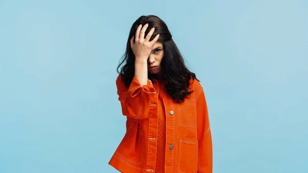 Unzufriedene junge Frau in orangefarbener Jeansjacke berührt Kopf isoliert auf blauem Grund — Stockfoto