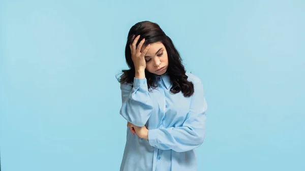 Незадоволена молода жінка в сорочці торкається голови і набиває щоки ізольовані на синьому — стокове фото