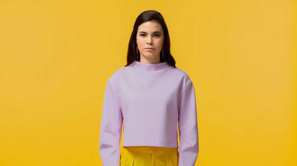 Brunette jeune femme en sweat-shirt violet debout et regardant la caméra isolée sur jaune — Photo de stock