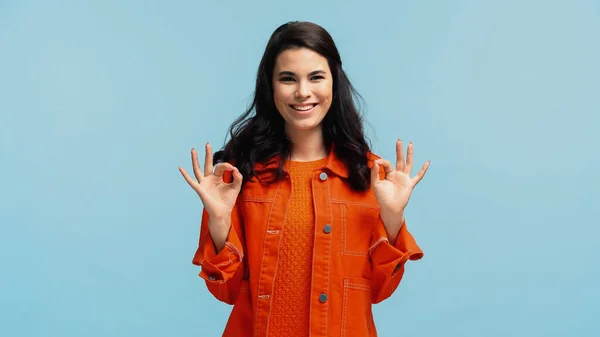 Feliz jovem mulher em casaco laranja mostrando ok isolado em azul — Fotografia de Stock