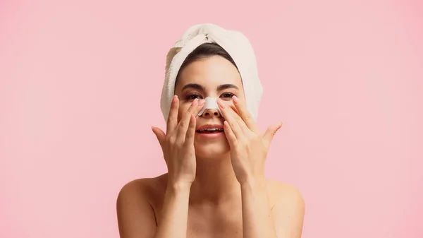 Young woman with towel on head applying patch on nose isolated on pink — Stock Photo