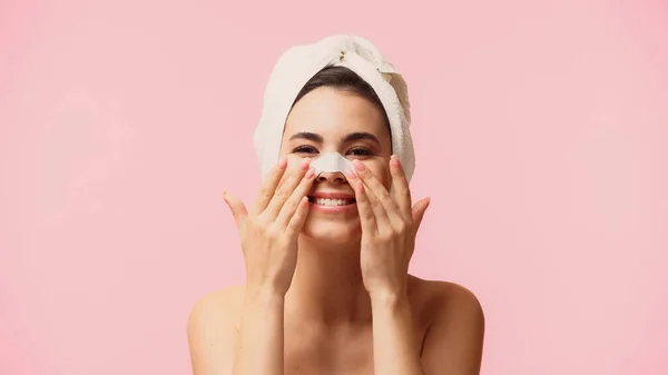 Cheerful young woman with towel on head applying patch on nose isolated on pink — Stock Photo