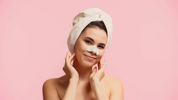 Jeune femme avec patch sur le nez et serviette sur la tête souriant isolé sur rose — Photo de stock