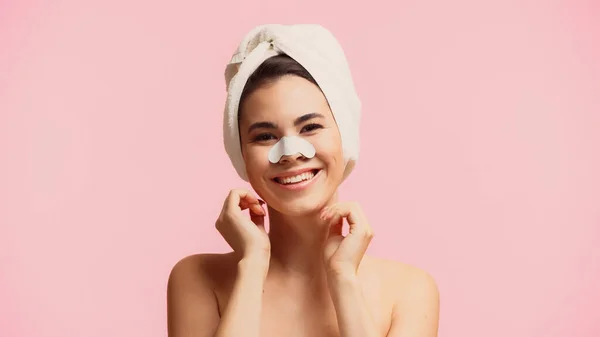 Alegre joven con toalla en la cabeza y parche en la nariz sonriendo aislado en rosa - foto de stock