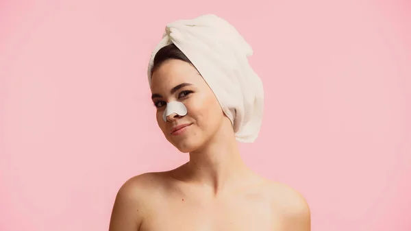 Mujer joven positiva con toalla en la cabeza y parche en la nariz sonriendo aislado en rosa - foto de stock