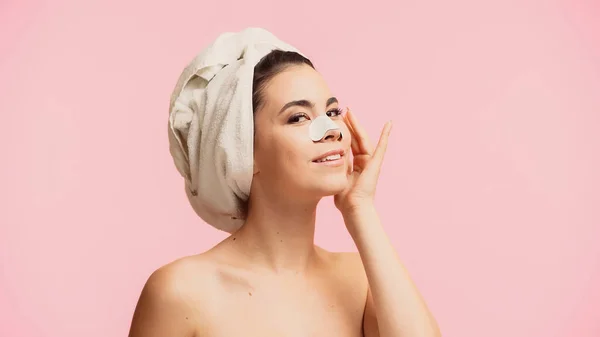 Alegre joven con toalla en la cabeza y parche en la nariz sonriendo aislado en rosa - foto de stock