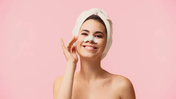 Happy young woman with towel on head and patch on nose smiling isolated on pink — Stock Photo