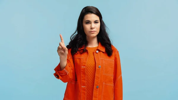 Skeptische junge Frau in orangefarbener Jacke, die mit dem Finger auf blau zeigt — Stockfoto