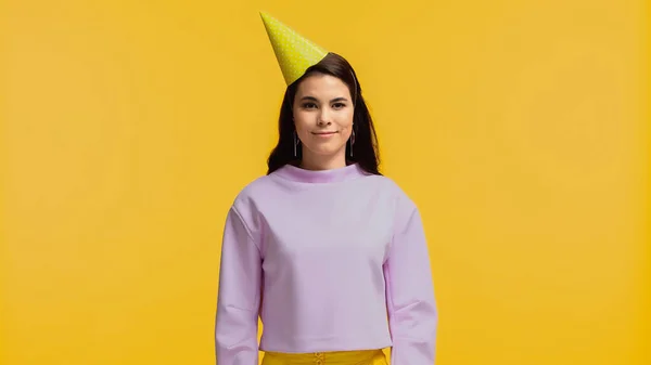 Smiling young woman in purple sweatshirt and party cap looking at camera isolated on yellow — Stock Photo