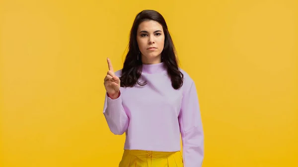 Mujer joven en sudadera púrpura apuntando con el dedo y mirando a la cámara aislada en amarillo - foto de stock