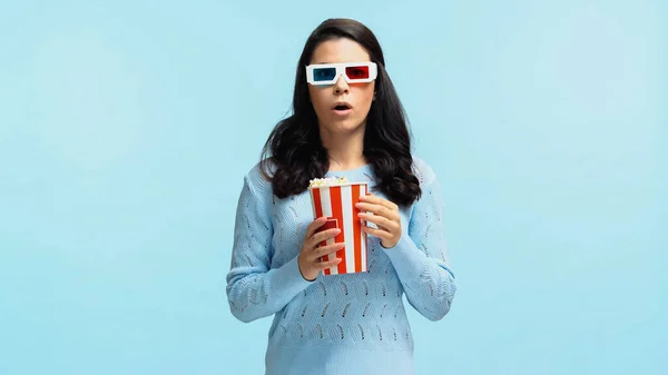 Surpresa jovem mulher em 3d óculos comer pipoca enquanto assiste filme isolado no azul — Fotografia de Stock