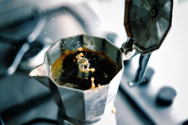 Coffee squirts out of an Italian moka pot with energy. Italian tradition and spitting out espresso. Splashes of black coffee spurting out from the spout and open moka pot stock photo. clipart