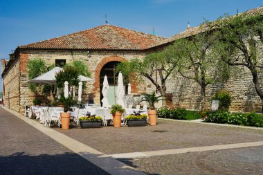 Facade of a restaurant in the historic streets of Lazise. Medieval architecture, cobblestones and olive trees. Reopening of outdoor activities after the pandemic.