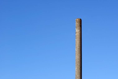 A simple concrete post. A long pole under a blue sky on a sunny day. Loneliness and minimalism.