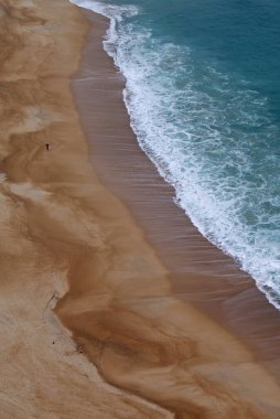 Man walks alone on a big beach in front of the ocean. Beautiful photo taken from above. A vast Portuguese ocean beach.