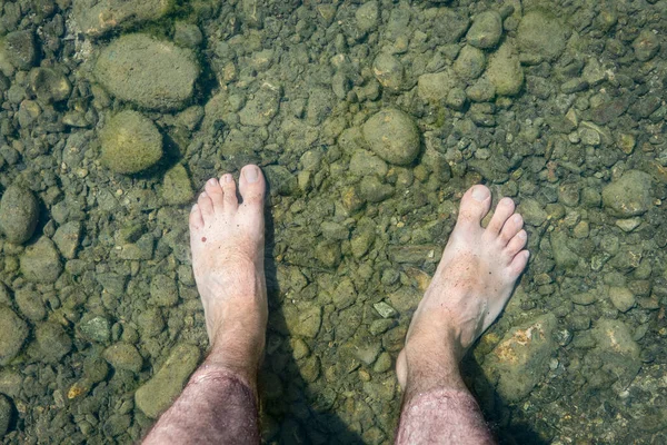Man\'s bare feet in clear water. Feet in cold water of a mountain lake. Foot pain on the stones and risk of infections.