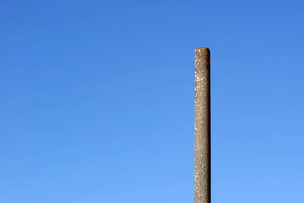 A simple concrete post. A long pole under a blue sky on a sunny day. Loneliness and minimalism.