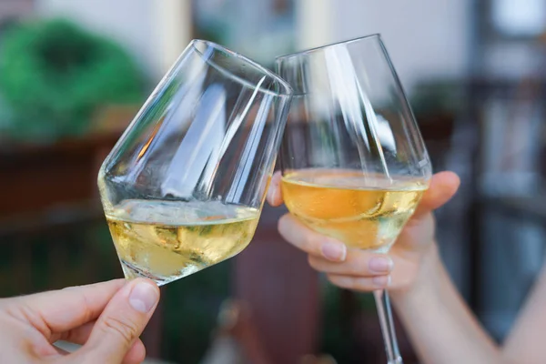 Two glasses of toasting wine. Hands toast with glasses of white wine during an aperitif. Moments of celebration with friends.