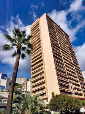 Monte Carlo, Monaco. Palm and tall skyscraper in Monte Carlo.Bottom view of a yellow skyscraper and plants. Blue sky, clouds and summer.
