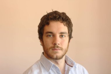 Portrait of an handsome young man with gray eyes, beard and brown hair.Model in front of a pink background.