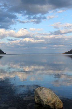 Panorama of Norwegian fjords with a rock in the foreground.Landscape in vertical photo.Reflection of the sky on the flat sea.