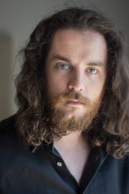 Man with gray eyes, beard and long brown hair. Serious expression.