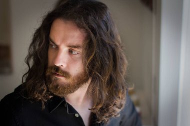 Portrait of man with gray eyes, beard and long brown hair. Macho man with serious expression. High testosterone.