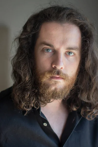 Man with gray eyes, beard and long brown hair. Serious expression.