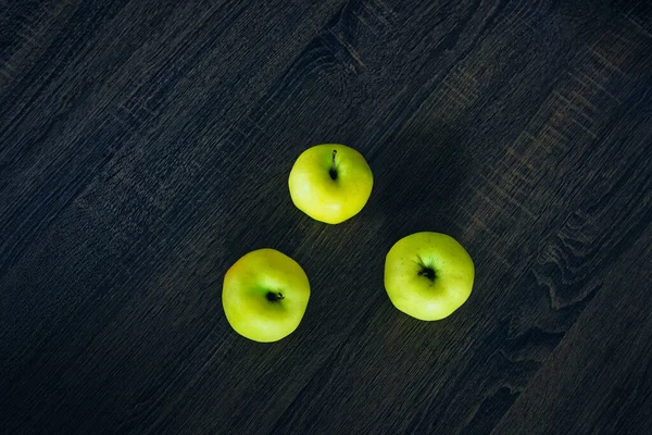 Green apples on a dark table.Three sweet fruits viewed from above on a dark painted wooden table. Wallpaper with natural products and fruits. Color contrast and minimalism.        