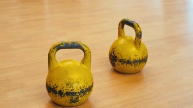 İki kullanılmış ve mahvolmuş sarı çaydanlık. Spor salonunun ahşap zemininde kullanılmış spor aletleri..