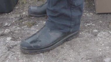 Shiny plastic boots. A farmer lifts his trousers showing his dirty black boot. Country life and work in the fields.