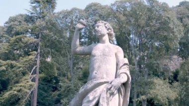 Moving shot around a statue. Greek deity viewed from below. Baroque style statue in an elegant garden of an italian villa. Visual art and sculpture.
