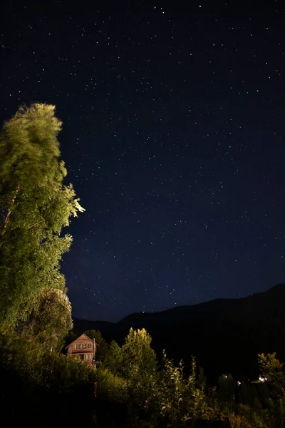 Dağlarda bir yaz gecesi. Tepedeki ahşap kulübe ve muhteşem yıldızlı gökyüzü.