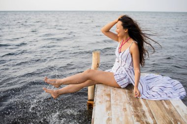 Güzel Asyalı kadın tek başına ahşap köprüde oturmuş açık okyanusa bakıyor..
