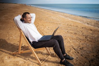 Plaj tatili sırasında tabletli genç bir adam. Dizüstü bilgisayarda çalışan serbest çalışan, güneşlenip uzanan biri..