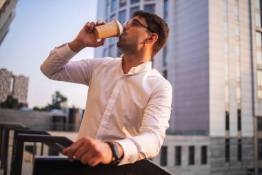 Şehirde cep telefonu kullanan ve kahve içen kendine güvenen genç bir işadamı.