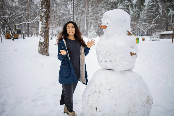 Aranyos Ázsiai Lány Kalapban Csinál Egy Hóembert Téli Parkban — Stock Fotó