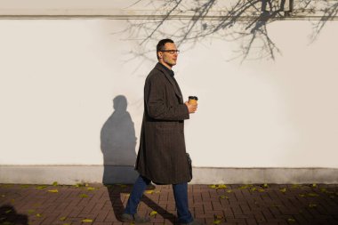 Gözlüklü, kahve ve evrak çantalı beyaz duvarlı bir iş adamının resmi..