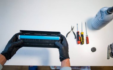 Hizmet merkezi ve atölye konsepti. Yazıcı için şarjör dolduran adam. Mürekkep şişesi beyaz masada. Tamirci eldivenle tamir ediyor..