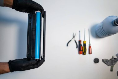 Hizmet merkezi ve atölye konsepti. Yazıcı için şarjör dolduran adam. Mürekkep şişesi beyaz masada. Tamirci eldivenle tamir ediyor..