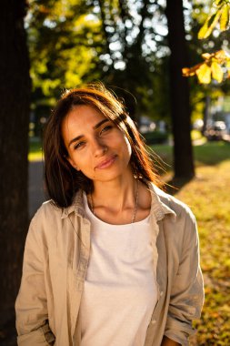 Gün batımında gülümseyen ve parka bakan güzel Amerikalı kadın portresi. Gülümseyen bir kızın açık hava portresi. Mutlu neşeli kız parka gülüyor. 