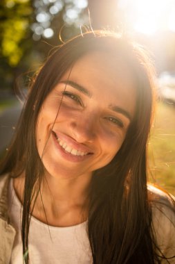Gün batımında gülümseyen ve parka bakan güzel Amerikalı kadın portresi. Gülümseyen bir kızın açık hava portresi. Mutlu neşeli kız parka gülüyor. 