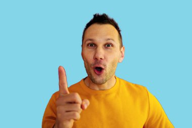 Gündelik giysiler giymiş genç yakışıklı bir adam başarılı bir fikri işaret ediyor. Heyecanlı ve mutlu. Bir numara..