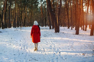 Kış ormanı kadını, uzun botlarıyla karda yürüyüşe çıkarıyor ağaçların arasında yürüyor.