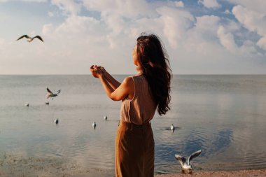 Genç kadın kış deniz sahilinde martıları besler. Kızla harika bir sahil sahnesi. Özgürlük, seyahat, uçma kavramı. Yaşam tarzı anı.