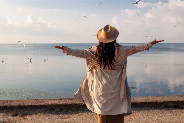 Young happy asian woman with hands in the air walks on the seaside in autumn. Seagulls flying on the beach.