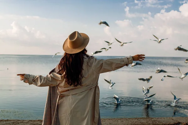 Young happy asian woman with hands in the air walks on the seaside in autumn. Seagulls flying on the beach.